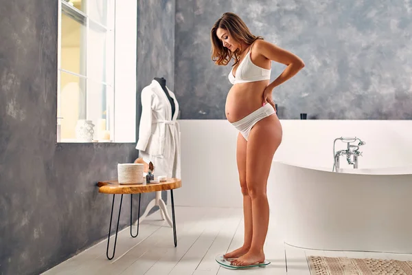 Banyoda Beyaz Çamaşırlı Hamile Bir Kadın Tartıdaki Ağırlığını Kontrol Ediyor — Stok fotoğraf