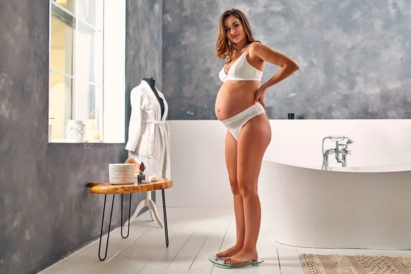Banyoda Beyaz Çamaşırlı Hamile Bir Kadın Tartıdaki Ağırlığını Kontrol Ediyor — Stok fotoğraf