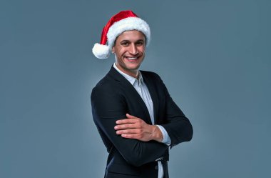 Attractive successful businessman in a jacket and shirt in a cap of Santa Claus in the studio on a gray background.