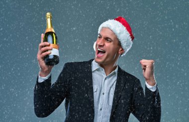 Successful man in a jacket and Christmas hat with a bottle of champagne celebrates New Year and say yes. Studio photo on a gray background .