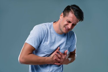 People, healthcare and health problem concept - unhappy young man having heart attack or heartache over gray  background.