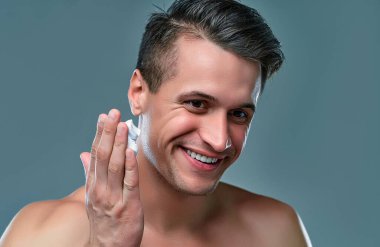Attractive man on a gray background uses shaving foam on his face. Men's care.