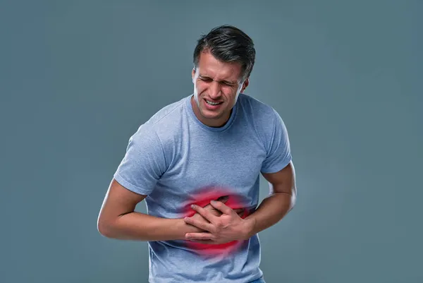 A man touching his stomach, on gray background with copy space. Stomach pain and others stomach disease concept.