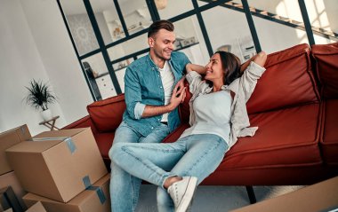 Evdeki oturma odasındaki kanepede oturan genç evli çift. Mutlu karı koca eğleniyor, yeni bir ev için sabırsızlanıyorlar. Taşınmak, ev almak, apartman konsepti..