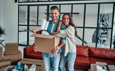 Evdeki oturma odasında evli genç bir çift eşyalarının olduğu kutuları açıyor. Mutlu karı koca eğleniyor, yeni bir ev için sabırsızlanıyorlar. Taşınmak, ev almak, apartman konsepti..