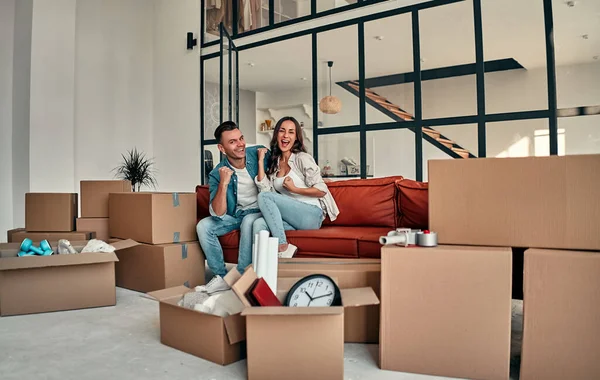 Evdeki oturma odasındaki kanepede oturan genç evli çift. Mutlu karı koca eğleniyor, yeni bir ev için sabırsızlanıyorlar. Yeni ev kavramının taşınması ve taşınması.