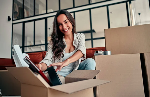 A young woman unpacking things from boxes in the living room in the house. Happy woman is looking forward to a new home. Moving, buying a house, apartment concept.