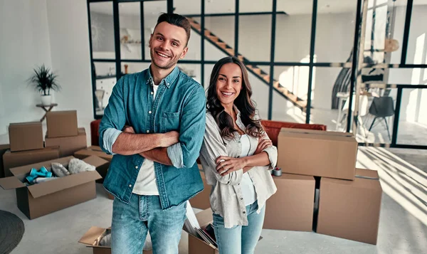 Young married couple in the living room at home. Against the background of unpacked boxes. Happy husband and wife are having fun, are looking forward to a new home. Moving, buying a house, apartment concept.