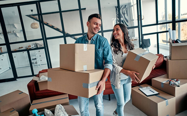 A young married couple in the living room in the house unpack boxes with things. Happy husband and wife are having fun, are looking forward to a new home. Moving, buying a house, apartment concept.