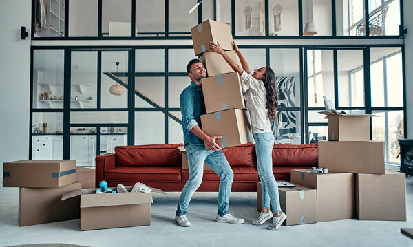 Moving, buying a house, apartment concept. Young couple with a bunch of falling boxes funny trying to catch them.