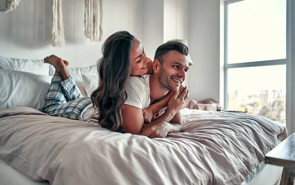 在家里的卧室里 一对快乐的年轻夫妇坐在床上 拥抱着 微笑着 — 图库照片