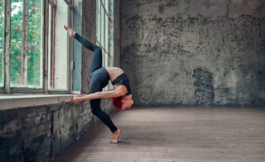 Siyah taytlı genç atletik kadın pencerenin yanında jimnastik yapıyor. Yoga konsepti. Kız esneme hareketleri yapıyor..