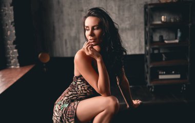 Deri koltuğun yanında poz veren kıvırcık saçlı güzel bir esmerin portresi..