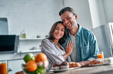 Mutfakta kahvaltıya hazırlanan romantik genç bir çift. Çekici genç bir kadın ve yakışıklı bir erkek aydınlık modern mutfakta dururken birlikte vakit geçirmekten zevk alıyorlar..