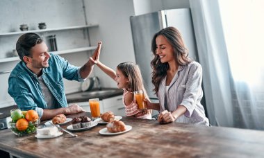 Mutfakta yemek yerken babaya beşlik çakmak. Mutlu aile, aydınlık modern mutfakta dururken birlikte vakit geçirmekten zevk alıyor..