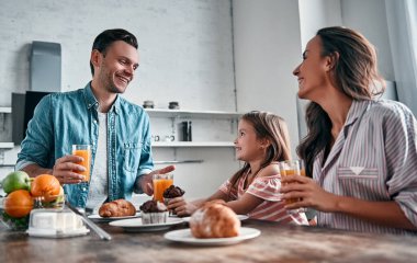 Anne, baba ve küçük güzel kızları mutfakta kahvaltı edip konuşuyorlar. Mutlu aile kavramı.