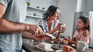 Anne, baba ve küçük güzel kızları mutfakta çay partisi yapıp sohbet ediyorlar. Babam ekmeğe tereyağı sürer. Mutlu aile kavramı.