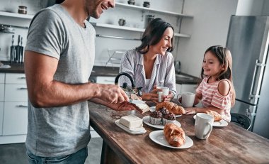 Anne, baba ve küçük güzel kızları mutfakta çay partisi yapıp sohbet ediyorlar. Babam ekmeğe tereyağı sürer. Mutlu aile kavramı.