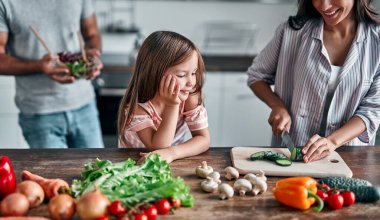Anne, baba ve kızı mutfakta yemek pişiriyor. Mutlu aile kavramı. Yakışıklı adam, çekici genç kadın ve tatlı küçük kızları birlikte salata yapıyorlar. Sağlıklı yaşam tarzı.