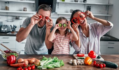 Anne, baba ve kızı mutfakta yemek pişiriyor. Mutlu aile kavramı. Yakışıklı adam, çekici genç kadın ve tatlı küçük kızları birlikte salata yapıyorlar. Sağlıklı yaşam tarzı.