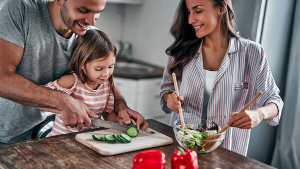 Mom, dad and daughter are cooking on kitchen. Happy family concept. Handsome man, attractive young woman and their cute little daughter are making salad together. Healthy lifestyle.