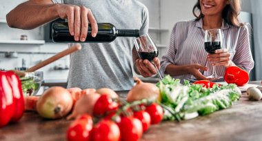 Romantik çift mutfakta yemek pişiriyor. Yakışıklı adam bardaklara şarap dolduruyor ve çekici genç bayan salata yaparken birlikte eğleniyor. Sağlıklı yaşam tarzı kavramı.
