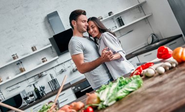 Mutfakta dans eden romantik bir çift. Yakışıklı adam ve çekici genç kadın salata yaparken birlikte eğleniyorlar. Sağlıklı yaşam tarzı kavramı.
