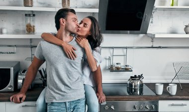 Romantik genç çift mutfakta öpüşüyor. Çekici genç bir kadın ve yakışıklı bir erkek aydınlık modern mutfakta dururken birlikte vakit geçirmekten zevk alıyorlar..