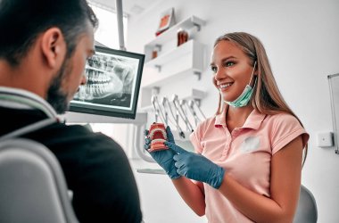 Diş modelini elinde tutan kadın dişçi klinikteki hastaya sağlık hizmetleri konseptini gösteriyor ve anlatıyor. Ağız hijyeninin tanıtımı..