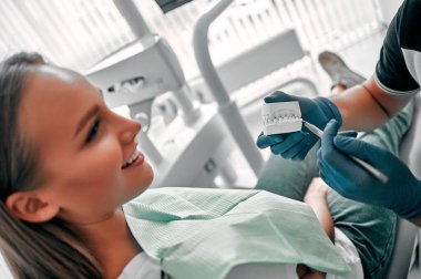 Diş modelini elinde tutan erkek dişçi klinikteki hastaya sağlık hizmetleri konseptini gösteriyor ve anlatıyor. Ağız hijyeninin tanıtımı..