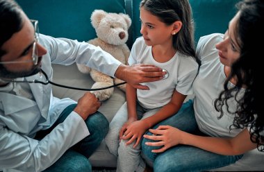 Güzel genç anne ve küçük kızı evde. Doktor steteskop kullanarak küçük bir hastayı muayene ediyor.