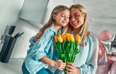 Mutlu anneler günü! Çocuk kızı anne tebrik ve onun çiçek Lale ve kartpostal verir. Anne ve kız gülümseyerek ve sarılma. Aile tatili ve beraberlik.