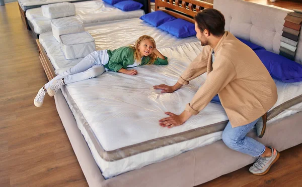一个年轻人 和他可爱的女儿躺在床上 在商店里试用床垫 看它是否柔软 买床和床上用品 — 图库照片