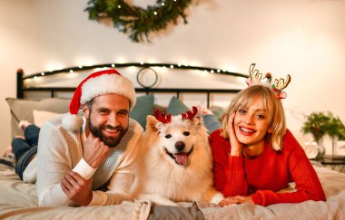 Mutlu Noeller ve mutlu yıllar! Güzel bir Noel ağacının yanında oturan tatlı bir kadın Noel Baba şapkalı beyaz tüylü bir köpeğe sarılıp bayramı bekliyor..