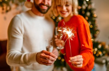 Mutlu Noeller ve mutlu yıllar! Noel Baba şapkalı ve ren geyiği boynuzları takmış bir çift Noel ağacının yanında, ellerinde maytaplar ve bir bardak şampanyayla tatil için bekliyorlar..