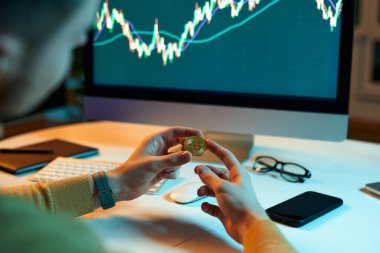Adam elinde altın paralar olan uluslararası değiş tokuşların finansal veritabanını kontrol ediyor ve kontrol ediyor. Kripto tüccar yatırımcı analisti dizüstü bilgisayar ekranına bakar, finansal grafik verilerini analiz eder