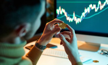 Adam elinde altın paralar olan uluslararası değiş tokuşların finansal veritabanını kontrol ediyor ve kontrol ediyor. Kripto tüccar yatırımcı analisti dizüstü bilgisayar ekranına bakar, finansal grafik verilerini analiz eder