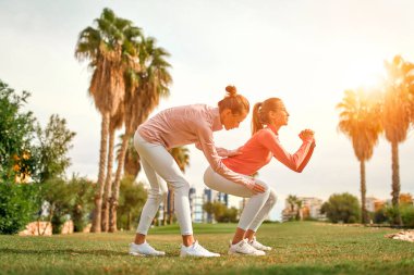Spor giyimli iki genç kadın bahçede palmiye ağaçlarının arka planına karşı egzersiz yapıyor. Spor ve Eğlence..