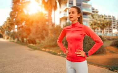 Sokakta palmiye ağaçlarının ve binaların önünde duran spor giysili narin genç kadın. Spor ve Eğlence..