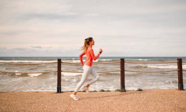 Deniz kenarında koşan spor giyimli narin bir genç kadın var. Sabah koşusu. Spor ve Eğlence..