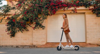 Çiçeklerle dolu bir kasabanın sokaklarında elektrikli scooterla gezen takım elbiseli genç iş kadını ya da bayan öğrenci..