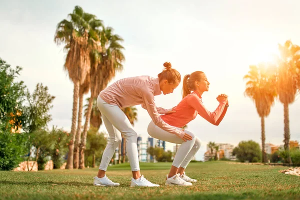 Spor giyimli iki genç kadın bahçede palmiye ağaçlarının arka planına karşı egzersiz yapıyor. Spor ve Eğlence..