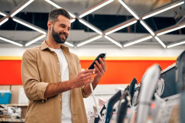 Sakallı stil sahibi bir adam, elektronik budama makineleri ve ustura ile vitrinde dikilirken bir seçim yapar. Mağazadan yeni bir budayıcı alıyorum..