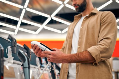 Sakallı stil sahibi bir adam, elektronik budama makineleri ve ustura ile vitrinde dikilirken bir seçim yapar. Mağazadan yeni bir budayıcı alıyorum..