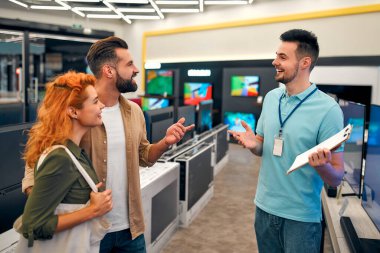 Genç mutlu çift yeni plazma TV almak için ev aletleri ve aletler mağazasına geldi. Satış danışmanı genç bir çiftin TV 'yi seçmesine yardımcı oluyor..