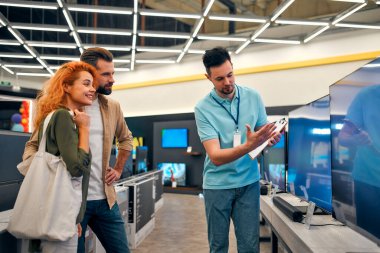 Genç mutlu çift yeni plazma TV almak için ev aletleri ve aletler mağazasına geldi. Satış danışmanı genç bir çiftin TV 'yi seçmesine yardımcı oluyor..