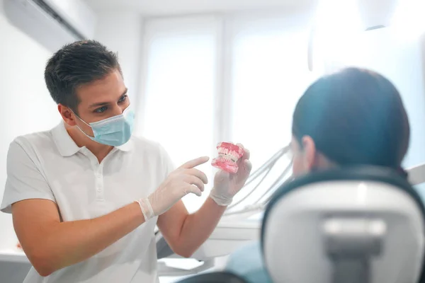 Joven Dentista Uniforme Blanco Máscara Médica Protectora Mostrando Modelo Mandíbula —  Fotos de Stock