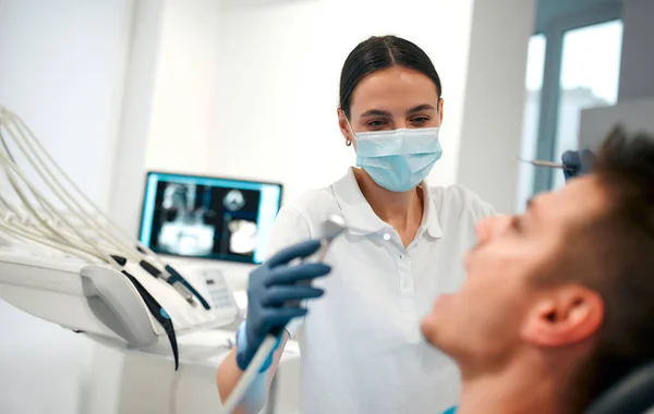 A young woman dentist in a medical mask examines a patient in a dental office with modern equipment. Caries treatment. Dentistry and dental care.