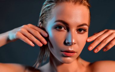 Çekici genç kız yüzüne dokunuyor. Gri bir arka planda mükemmel cilde sahip sarışın bir kızın fotoğrafı. Güzellik ve cilt bakımı kavramı.