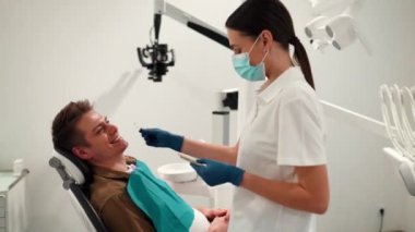 İlaç, diş hekimliği ve sağlık sigortası konsepti - diş renginde numunelerle bir dişçinin diş sağlığı kliniğinde erkek bir hastanın dişleri için gölge seçmesi.